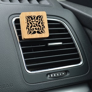 May include: A wooden car air freshener with a decorative cutout design. The air freshener is attached to a car's air vent.