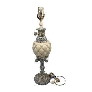 May include: A table lamp featuring a cream-colored, diamond-quilted ceramic body with a weathered gray and white finish on the metal base and neck. The lamp includes a metal socket, a decorative turn knob, and a beige electrical cord.