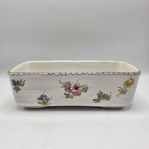 May include: A rectangular ceramic planter with a white base and a scalloped green rim. The exterior features hand-painted floral motifs in shades of pink, blue, and yellow with green leaves, set against a subtle, light gray brushstroke texture.
