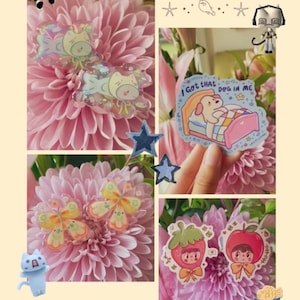 May include: A collection of colorful stickers featuring a dog in a bed with the text I Got That DOG IN ME, butterfly shapes, and characters wearing strawberry and apple costumes, all displayed against a background of pink chrysanthemum flowers.