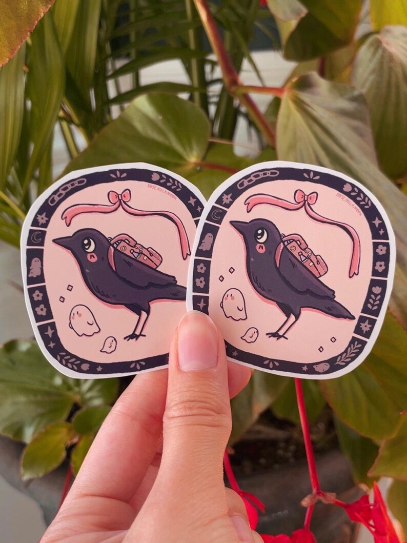 May include: Two black crow stickers with pink ribbons and small ghost illustrations. The crows are carrying small bags with pink accents. The stickers have a black and white border with a floral design.