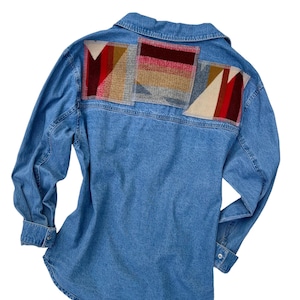 May include: A blue denim shirt with a patchwork design on the back. The patchwork is made of different colored fabrics, including red, brown, and beige.