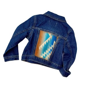 Puede incluir: Una chaqueta vaquera azul con un patrón geométrico colorido en la espalda. El patrón es en tonos de azul, marrón y blanco.