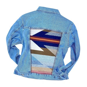 May include: A blue denim jacket with a colourful geometric patterned fabric patch on the back.
