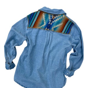 May include: A light blue denim shirt with a colorful geometric pattern on the back. The pattern is in shades of blue, brown, and turquoise.