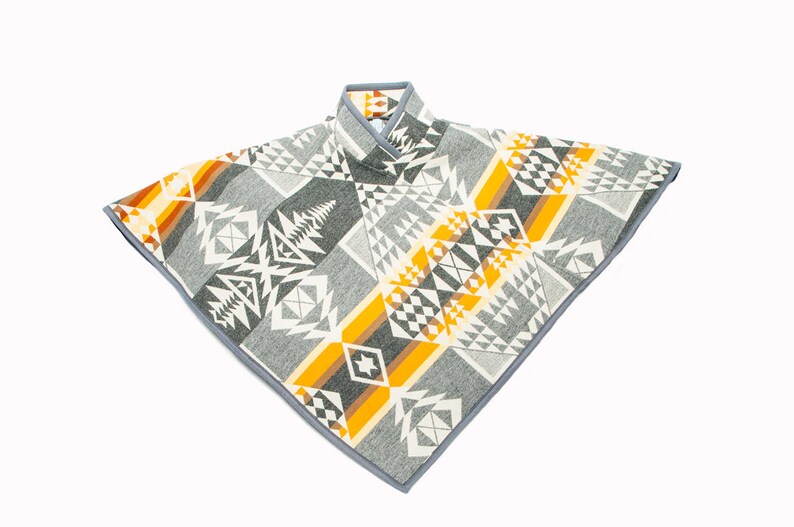 May include: A grey, white and yellow patterned poncho with a grey trim. The poncho has a geometric design with a Native American inspired pattern.