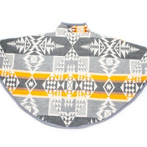 May include: A grey and yellow patterned poncho with a geometric design. The poncho has a high neck and a rounded hem.