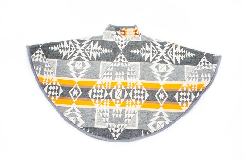May include: A grey and yellow patterned poncho with a geometric design. The poncho has a high neck and a rounded hem.