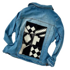 May include: A blue denim jacket with a black and white geometric patterned patch sewn on the back.