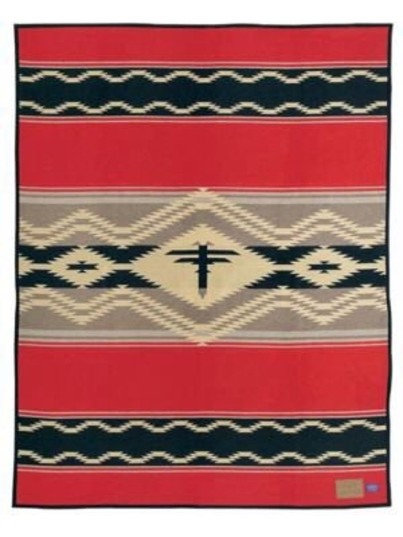 Puede incluir: Una manta rectangular con un fondo rojo vibrante y bandas horizontales de patrones geom&eacute;tricos en negro y crema. Una forma de diamante central contiene un motivo de p&aacute;jaro negro estilizado, flanqueado por intrincadas l&iacute;neas en zigzag en tonos beige.