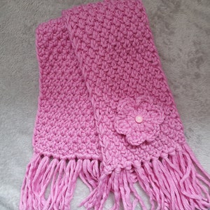 May include: A pink crocheted scarf with a flower accent and fringe.