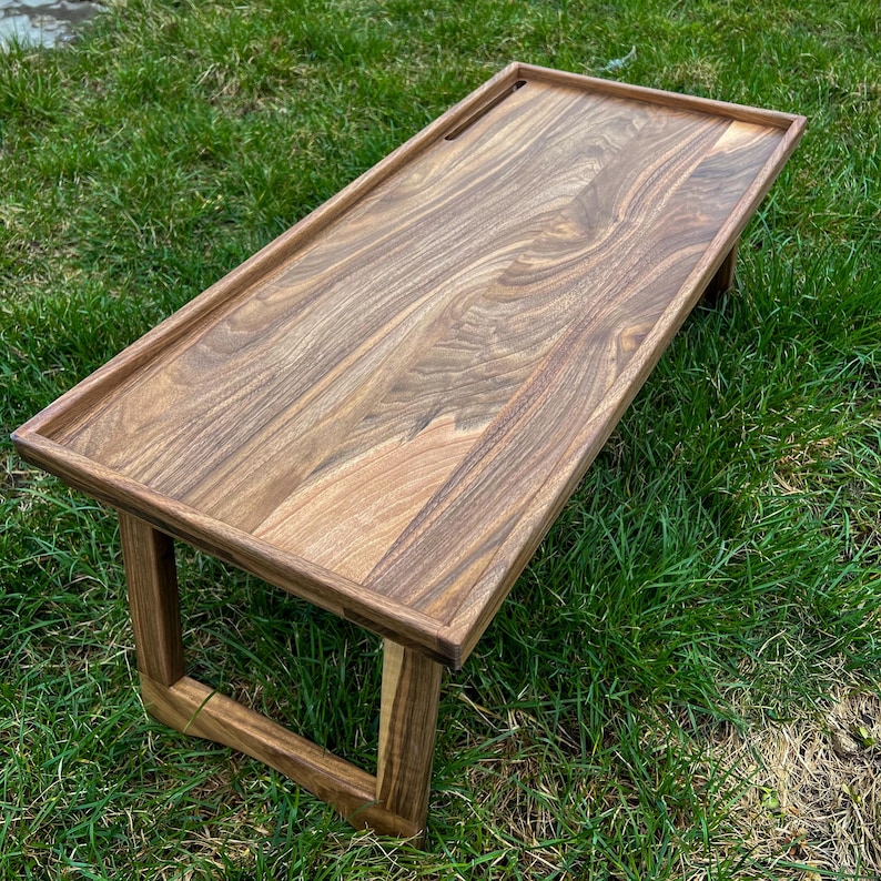 May include: A wooden table with a rectangular top and a simple, modern design. The table has a natural wood finish and is made of solid wood. The table is perfect for use as a laptop desk or a small coffee table.