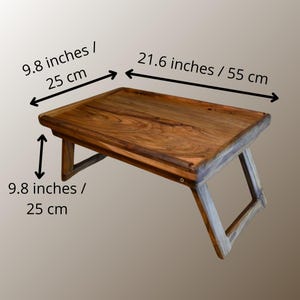 May include: A wooden lap desk with folding legs. The desk is rectangular, with dimensions of 21.6 inches long, 9.8 inches wide, and 9.8 inches high. The wood has a natural grain and a warm brown color.