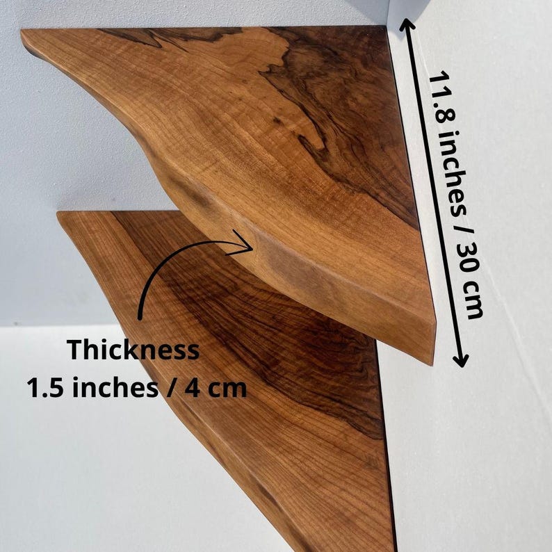 May include: Two wooden floating shelves with a natural wood grain finish. Each shelf is triangular, with a curved front edge. The shelves are 11.8 inches (30 cm) long and 1.5 inches (4 cm) thick. The shelves are mounted on a white wall.