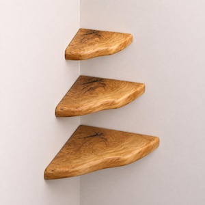 Peut inclure: Trois étagères d'angle triangulaires en bois naturel brun clair avec des motifs de grain visibles et des détails de nœuds sombres et irréguliers. Chaque étagère présente un bord avant incurvé et lisse fixé contre un angle de mur.