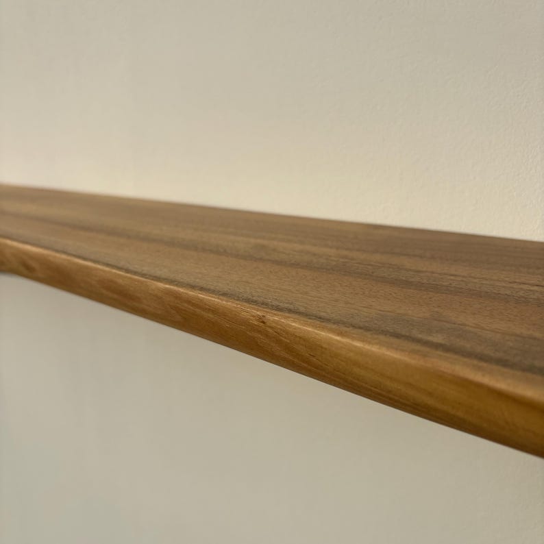 May include: A solid wood floating shelf with a natural finish. The shelf is a warm brown color and has a smooth, polished surface. The shelf is mounted on a white wall.