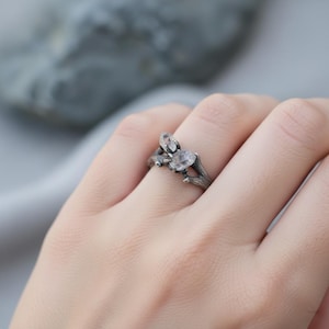 Peut inclure: Bague argent&eacute;e avec un motif de brindille orn&eacute;e de trois pierres pr&eacute;cieuses ovales et transparentes. La bague est port&eacute;e sur un doigt, mettant en valeur les d&eacute;tails.