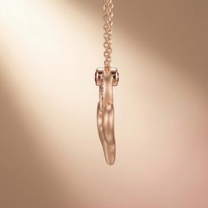 May include: A rose gold necklace with a heart-shaped pendant. The pendant is embellished with small pink gemstones and a larger pink gemstone at the top. The chain is also rose gold.