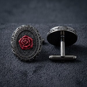 May include: A pair of oval cufflinks featuring a dark gunmetal finish with an intricate engraved border and a central raised red rose motif. The design includes a polished metallic post and a hinged toggle mechanism for secure fastening on a shirt cuff.