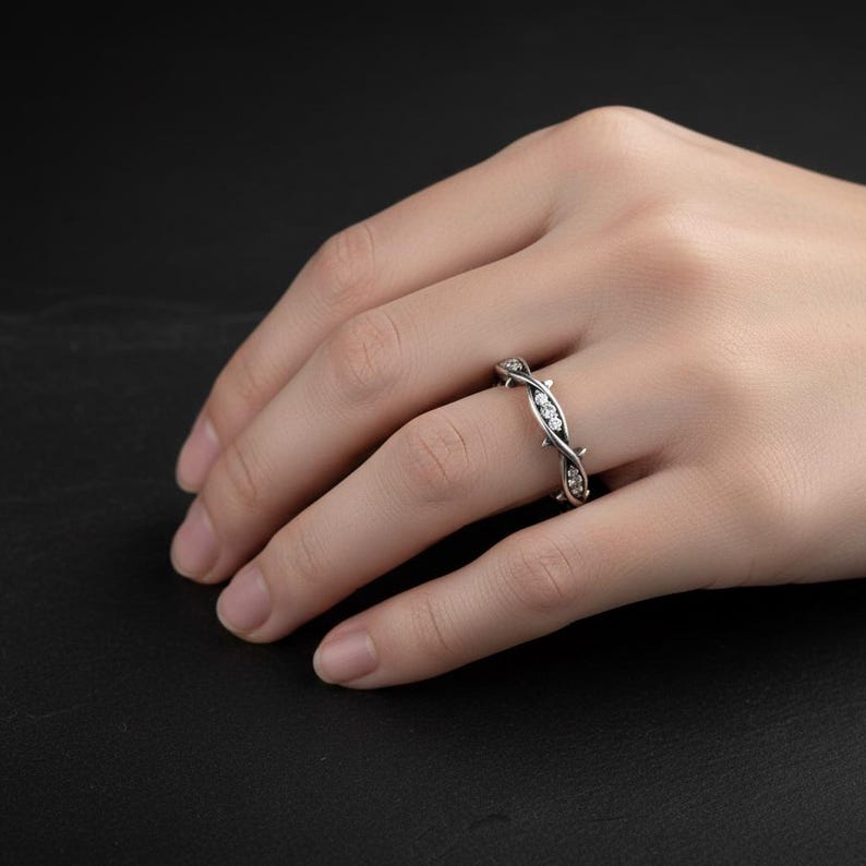 May include: A silver-toned ring featuring a twisted vine or thorn-like design with small, clear, round-cut stones embedded along the band. The metal has a darkened, oxidised finish in the recessed areas to highlight the intricate texture.