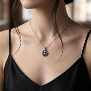 Peut inclure: Un collier argent&eacute; dot&eacute; d'un pendentif circulaire orn&eacute; d'un motif de cr&acirc;ne d&eacute;taill&eacute; et d'une petite pierre pr&eacute;cieuse ovale bleu clair plac&eacute;e au-dessus du cr&acirc;ne. Le pendentif est suspendu &agrave; une fine cha&icirc;ne argent&eacute;e d&eacute;licate.