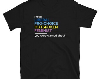 May include: A black short-sleeved t-shirt featuring the white text I'm the, followed by the words LIBERAL in blue, PRO-CHOICE in light blue, OUTSPOKEN in yellow, and FEMINIST in purple, with the white text you were warned about below.