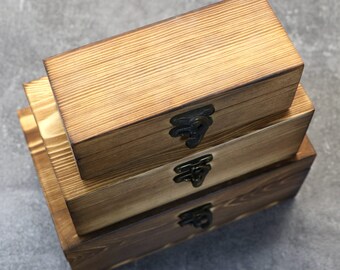 May include: Three wooden boxes stacked on top of each other. The boxes are made of light brown wood and have a natural wood finish. Each box has a metal latch on the front.