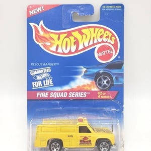 Peut inclure: Un camion de pompier jouet en métal moulé sous pression Hot Wheels Fire Squad Series jaune, modèle Rescue Ranger, dans son emballage d'origine. L'emballage est bleu avec des accents rouges et blancs, et présente le logo Hot Wheels.