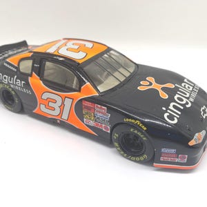 May include: A black and orange die-cast stock car model featuring the number 31 on the roof and sides. The vehicle displays Cingular Wireless branding, a Chevrolet logo on the hood, and various sponsor decals including Goodyear and 3M.
