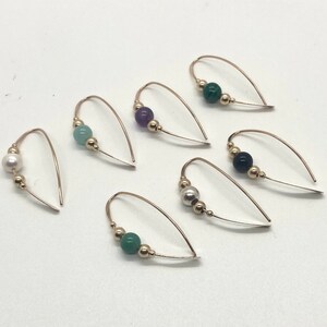 May include: Six pairs of gold hoop earrings with different colored gemstone beads. The beads are green, purple, white, and black.