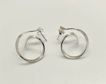 May include: A pair of silver hoop earrings with a unique twisted design. The earrings are made from a single piece of metal that is twisted into a circle.