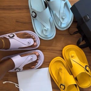 Könnte beinhalten: Drei Paar klobige Zehentrenner-Sandalen mit Plateau in Hellblau, Lavendel und Gelb, jeweils mit einem breiten Riemen und einer dunklen runden Schnalle. Der Text "POV: you just created a unique chunky platform" ist oben im Bild zu sehen.