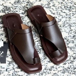 May include: A pair of brown leather sandals with a toe strap and an open back. The sandals have a simple design and are made of high-quality leather.