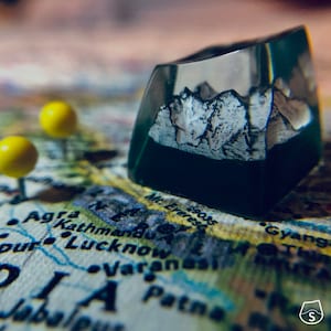 May include: A clear resin keycap with a mountain range design inside. The keycap is sitting on a map of India with push pins.