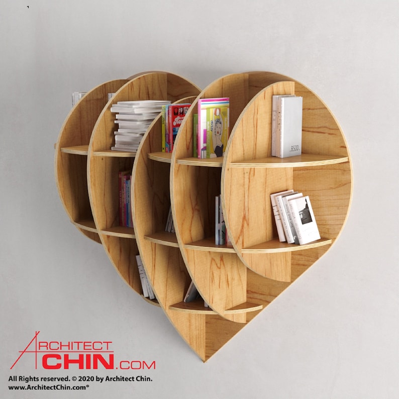 Pu&ograve; includere: Una libreria in legno a forma di cuore con pi&ugrave; ripiani. I ripiani sono pieni di libri e riviste. La libreria &egrave; montata su una parete bianca.