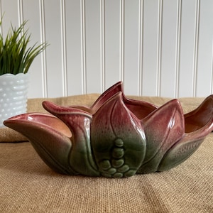 May include: A ceramic planter shaped like a flower with pink and green glaze. The planter has a wide, shallow bowl and a raised center section.