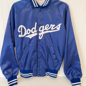 May include: A royal blue satin jacket with the word "Dodgers" in white script across the chest. The jacket has a button-up front, blue and white striped cuffs and collar, and a white and blue striped collar.