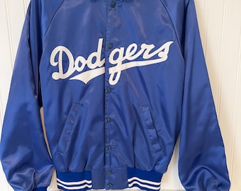 以下が含まれることがあります： 胸に白い筆記体で「Dodgers」の文字が入った、ロイヤルブルーのサテンジャケット。 ジャケットはボタン留め、青と白のストライプのカフスと襟、白と青のストライプの襟が付いています。