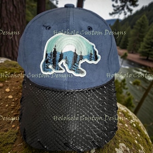Könnte beinhalten: Marineblaue Baseballkappe mit schwarzem Schirm in Schlangenlederoptik. Die Kappe hat ein gesticktes Bärenmotiv mit einer Berg- und Waldszene in Blau- und Weißtönen. Der Text "Holoholo Custom Designs" ist auf der Kappe aufgedruckt.