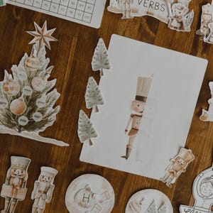 Peut inclure: Illustrations &agrave; l'aquarelle de d&eacute;corations de No&euml;l, dont un sapin, des casse-noisettes, des boules &agrave; neige et un ch&acirc;teau avec le mot "VERBS". Les &eacute;l&eacute;ments sont dispos&eacute;s sur une surface en bois.