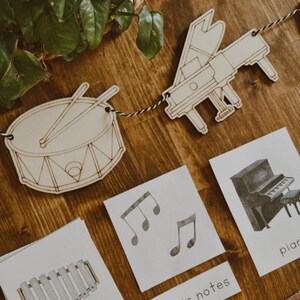 Pu&ograve; includere: Sagome di tamburo e pianoforte in legno legate insieme con un cordoncino bianco e nero. Sono visibili anche carte con note musicali, uno xilofono e un pianoforte. Le parole "note musicali" e "xilofono" sono stampate sulle carte.