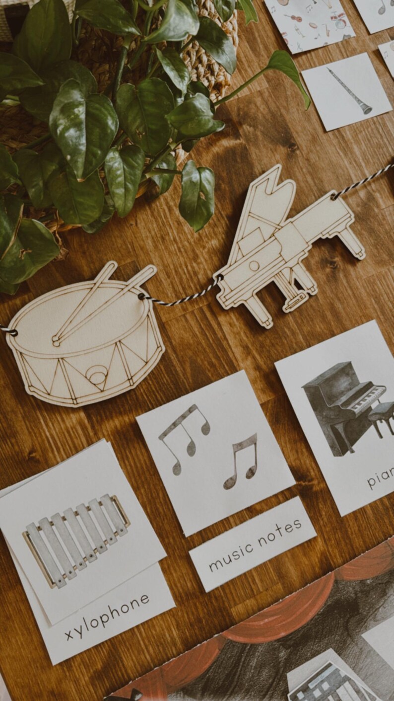 Pu&ograve; includere: Sagome di tamburo e pianoforte in legno legate insieme con un cordoncino bianco e nero. Sono visibili anche carte con note musicali, uno xilofono e un pianoforte. Le parole "note musicali" e "xilofono" sono stampate sulle carte.