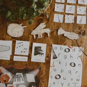 Pu&ograve; includere: Sagome di strumenti musicali in legno e flashcard con note musicali, un pianoforte e una tromba. Uno striscione di strumenti musicali in legno &egrave; appeso sopra le flashcard. &Egrave; visibile anche un poster con l'alfabeto.