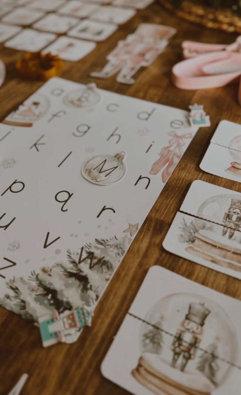Peut inclure: Une table en bois pr&eacute;sente des cartes &eacute;ducatives avec l'alphabet, des illustrations sur le th&egrave;me de No&euml;l et des pi&egrave;ces de puzzle. Les cartes pr&eacute;sentent des lettres, un motif de sapin de No&euml;l et une boule &agrave; neige avec un casse-noisette. La palette de couleurs comprend le blanc, le vert et le marron.