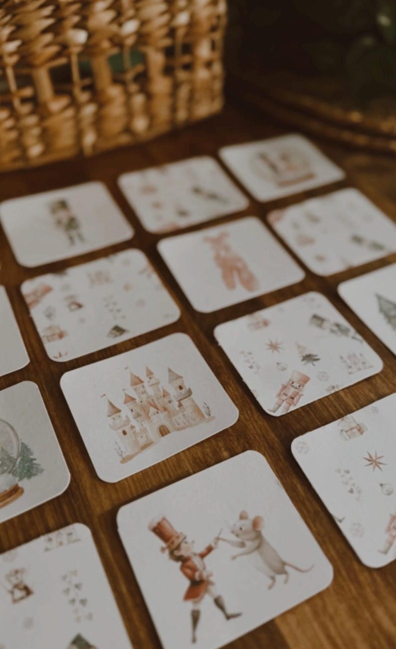 Peut inclure: Ensemble de cartes carr&eacute;es avec des illustrations &agrave; l'aquarelle d'un ch&acirc;teau, d'un casse-noisette, d'une ballerine et d'autres images sur le th&egrave;me des f&ecirc;tes. Les cartes sont dispos&eacute;es sur une surface en bois, avec un panier en osier en arri&egrave;re-plan.