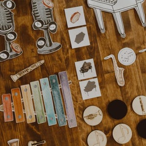 Pu&ograve; includere: Ritagli e illustrazioni di strumenti musicali in legno, tra cui uno xilofono, un pianoforte, un microfono e note musicali, sono disposti su una superficie di legno. La parola "big" &egrave; visibile.