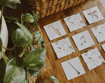 Può includere: Ritagli di strumenti musicali in legno e flashcard con illustrazioni di strumenti musicali sono disposti su una superficie di legno. Un cestino di vimini contiene altri strumenti in legno. Una pianta è nell'angolo.