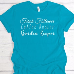 Puede incluir: Una camiseta azul turquesa con texto blanco que dice "Torah Follower Coffee Bustler Garden Keeper".