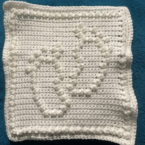 May include: White crocheted square with a textured pattern of raised dots. The square is made with a single crochet stitch and has a border of single crochet stitches.