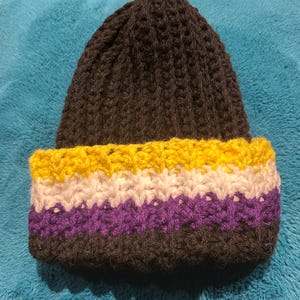 Op de afbeelding: Zwarte gebreide beanie met een gele, witte en paarse streep aan de rand.